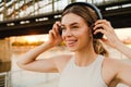 Young smiling woman listening music with headphones while standing on embankment Royalty Free Stock Photo