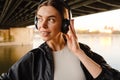 Young smiling woman listening music with headphones while standing on embankment Royalty Free Stock Photo