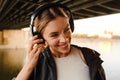 Young smiling woman listening music with headphones while standing on embankment Royalty Free Stock Photo