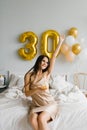 Young smiling woman with long hair lies in bed with a cake on a plate and a candle and celebrates her birthday Royalty Free Stock Photo