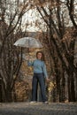 Young smiling woman with long hair poses in fall park. Woman in blue sweater and pants and holds transparent umbrella Royalty Free Stock Photo