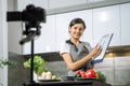 Young smiling woman nutritionist showing a comparative table of calorie foods and recording video on a camera in the kitchen