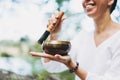 Young smiling woman playing on the brass Tibetan singing bowl outdoor. Sound therapy and meditation Royalty Free Stock Photo