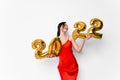 Young smiling woman in red cocktail dress with bright make-up celebrating New Year 2022 and holding golden balloons 2022 Royalty Free Stock Photo