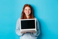 Young smiling woman with red hair and freckles showing computer screen, holding laptop and demonstrate online promo