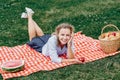 Young smiling woman relaxing outdoors and having a picnic, she is lying down on a red cell blanket on grass in meadow Royalty Free Stock Photo