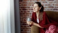 Young smiling woman relaxing on sofa with cup of tea at big window. Female resting at home, lifestyle and relaxation Royalty Free Stock Photo