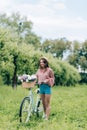 young smiling woman with retro bicycle with wicker basket full of flowers