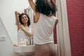 Positive woman shaving her armpits while looking at herself in the mirror in bathroom Royalty Free Stock Photo