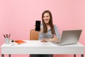 Young smiling woman showing on camera mobile phone with blank empty screen work at white desk with contemporary pc Royalty Free Stock Photo