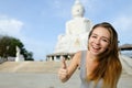 Young smiling woman showing thumbs up, white Buddha statue in Phuket in background.