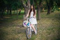Young smiling woman sits on a bicycle with a basket of flowers in the evening in the park. Royalty Free Stock Photo