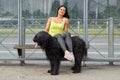 Cheerful girl put her legs on black briard on bus stop.