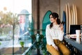 Young smiling woman sitting in cafe at table,looking out window, holding smartphone, listening to music on headphones. Lifestyle Royalty Free Stock Photo