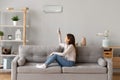 Young smiling woman sitting on couch switching on air conditioner Royalty Free Stock Photo