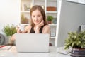 Young smiling woman sitting at desk, drinking coffee at home in the morning, working on laptop computer in the living room Royalty Free Stock Photo