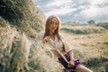 Young smiling woman is sitting near haystack on meadow. Royalty Free Stock Photo