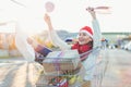 Young smiling woman sitting in shopping cart with a lot of gift boxes wearing red Santa Christmas hat Royalty Free Stock Photo