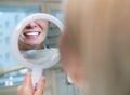 Young smiling woman sitting in stomatology clinic chair and looked at mirror evaluating her teeth reflection after Tooth whitening Royalty Free Stock Photo