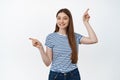 Young smiling woman suggest two options, pointing fingers up and left, showing variants, standing over white background Royalty Free Stock Photo