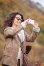 Young smiling woman take photo with mobile phone in autumn forest. Royalty Free Stock Photo