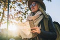 Young smiling woman travels in hat and eyeglasses stands on city street, holding map in her hands.Hipster girl walks. Royalty Free Stock Photo