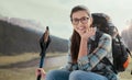 Young smiling woman trekking on the mountains and having a relaxing break, she is sitting and holding hiking poles