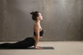 Young smiling woman in Urdhva mukha shvanasana pose, grey studio