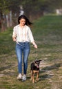 Young smiling woman walking her dog on a leash on a beautiful sunny day in park Royalty Free Stock Photo