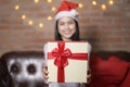 Young smiling woman wearing red Santa Claus hat showing a gift box on Christmas day, holiday concept Royalty Free Stock Photo