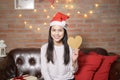 Young smiling woman wearing red Santa Claus hat showing a heart shaped model on Christmas day, holiday concept Royalty Free Stock Photo