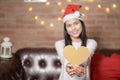 Young smiling woman wearing red Santa Claus hat showing a heart shaped model on Christmas day, holiday concept Royalty Free Stock Photo