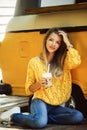 Beautiful smiling woman is wearing yellow sweater drinking coffee latte near old retro bus Royalty Free Stock Photo