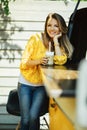 Pretty smiling woman is wearing yellow sweater drinking coffee latte near old retro bus, food and drink concept Royalty Free Stock Photo