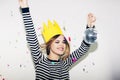 Young smiling woman on white background celebrating party, wearing stripped dress and yellow paper crown, happy dynamic