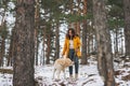 Young smiling woman in yellow jacket with big kind white dog Labrador walking in winter forest Royalty Free Stock Photo