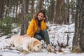 Young smiling woman in yellow jacket with big kind white dog Labrador walking in winter forest Royalty Free Stock Photo