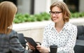 Smiling woman with digital tablet in hand discussing startup with business partner in outdoor cafe Royalty Free Stock Photo