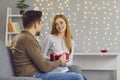 Young smiling woman girlfiend sitting and getting present box with ribbon from loving man