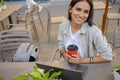 Beautiful entrepreneur using laptop during lunch in outdoor cafe, elegant businesswoman holding coffee cup working in city street.