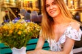 Young woman sitting at street cafe near flowers and green plants. Concept of cozy place in open air and resting. Royalty Free Stock Photo