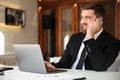 Young smliing bearded business man in black suit talking on mobile phone, looking aside in office Royalty Free Stock Photo