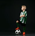 Young football school student, kid boy in red white uniform stands with ball under his foot and looks aside Royalty Free Stock Photo