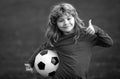 Young soccer player in sportswear with soccer ball show thumbs up success sign. Cheerful little boy enjoy soccer