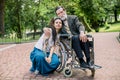 Young social worker or granddaughter takes care about senior man in wheelchair at walk in a park, smiling and embracing