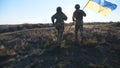 Young soldiers of ukrainian army running with lifted national banner on field. Military woman and man in camouflage Royalty Free Stock Photo