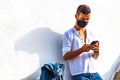 Young solo traveller leaning at a white wall with trolley bag using smartphone chatting online waiting bus or train wearing