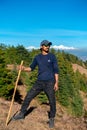 Young solo trekker with bamboo walking stick in the Himalayan hills, backdrop of glacial peaks. Uttarakhand, India. Adventurous