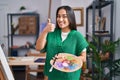 Young south asian woman holding painter palette smiling happy and positive, thumb up doing excellent and approval sign Royalty Free Stock Photo