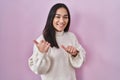 Young south asian woman standing over pink background pointing to the back behind with hand and thumbs up, smiling confident Royalty Free Stock Photo